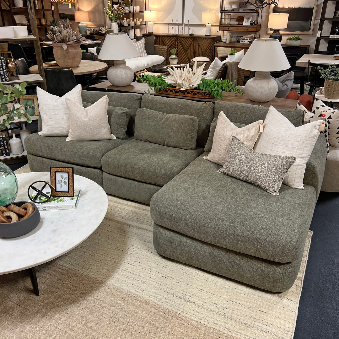 A green Monterey sectional sofa with multiple cushions, displayed in a showroom with decorative items on the sides.