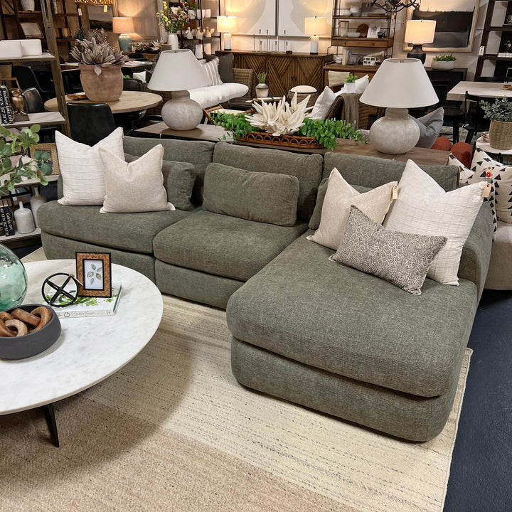 A green Monterey sectional sofa with multiple cushions, displayed in a showroom with decorative items on the sides.