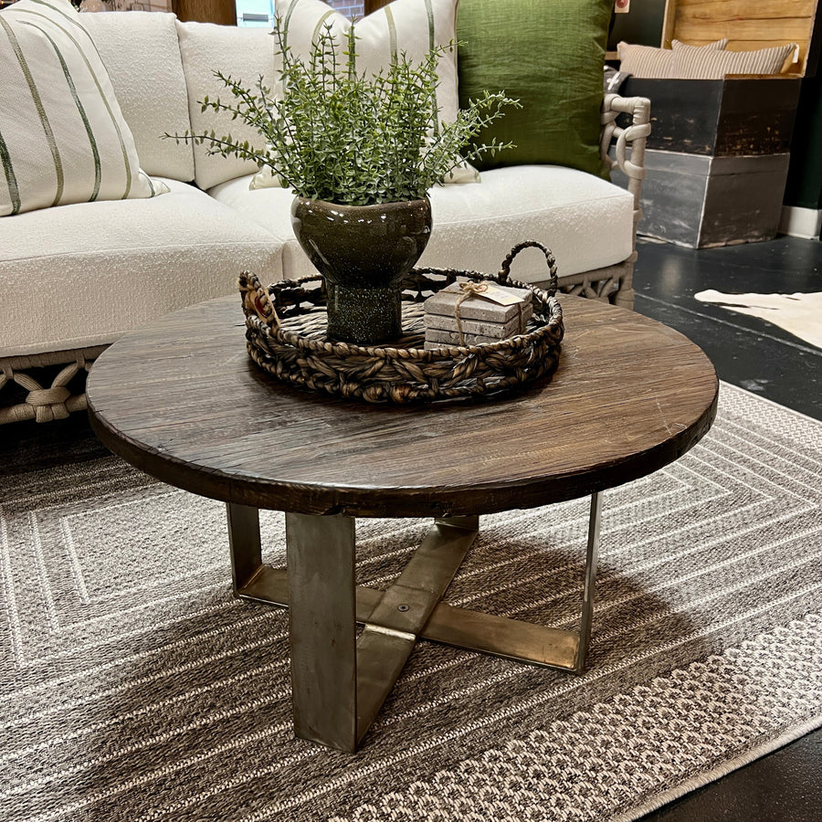 Round wooden coffee table with decorative items in a living room setting.