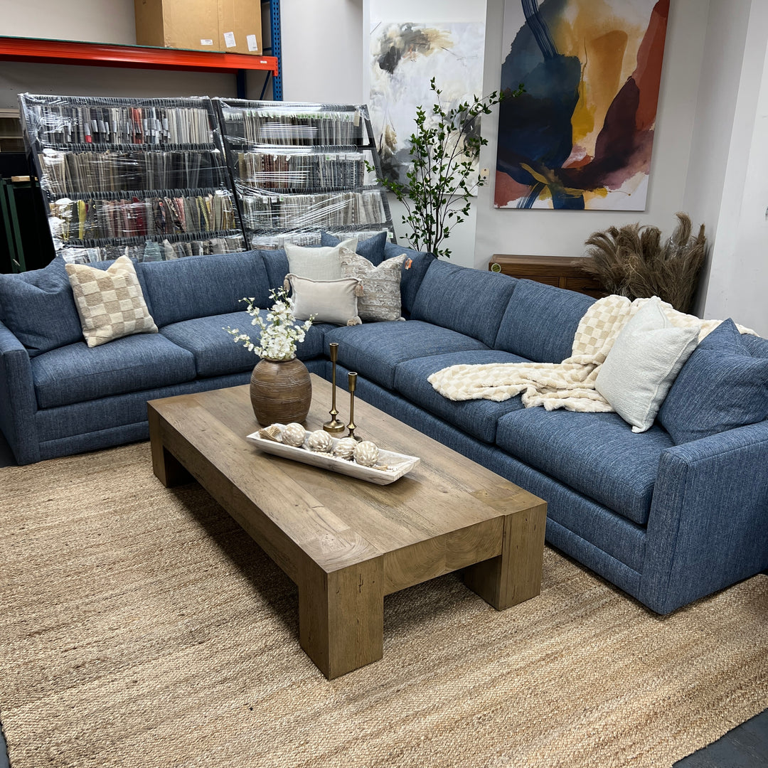 A traditional 'L-shaped' sectional sofa in blue performance fabric, arranged in a showroom setting with a wooden coffee table in front.