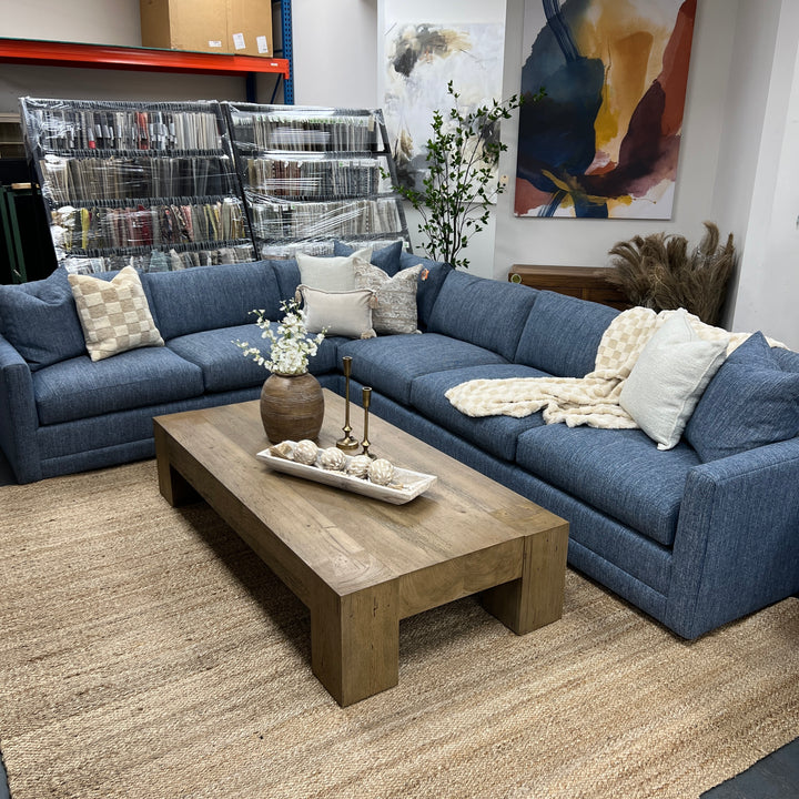 A traditional 'L-shaped' sectional sofa in blue performance fabric, arranged in a showroom setting with a wooden coffee table in front.